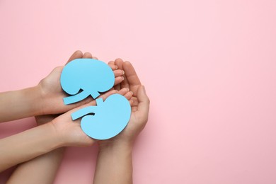 Photo of People holding paper cutout of kidneys on pink background, top view. Space for text