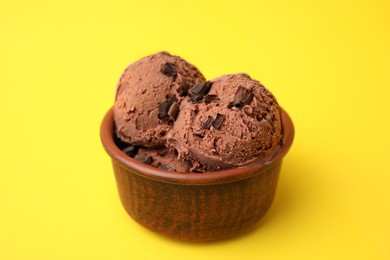 Photo of Bowl of tasty ice cream with chocolate chunks on yellow background, closeup