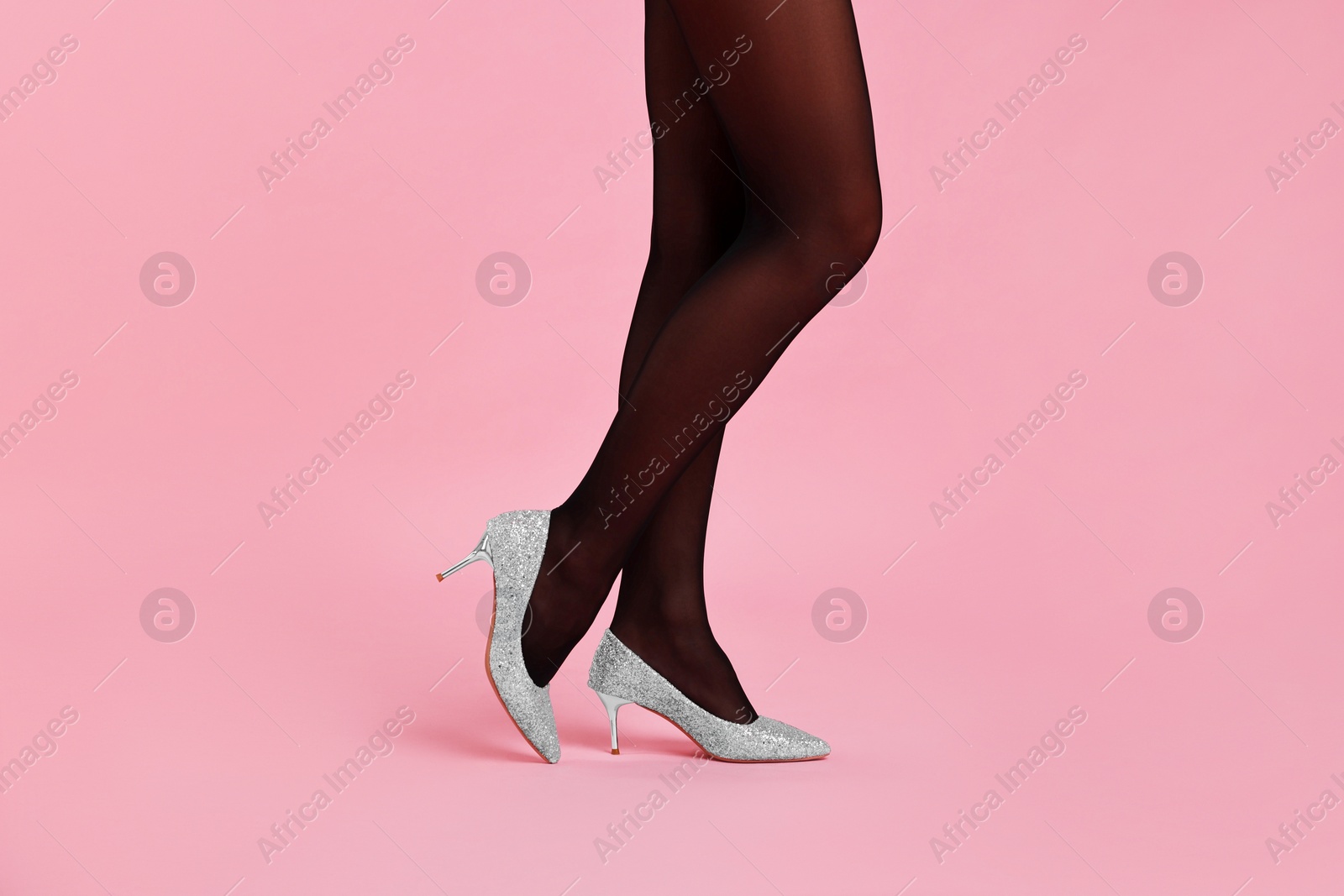 Photo of Woman with beautiful long legs wearing black tights and stylish shoes on pink background, closeup