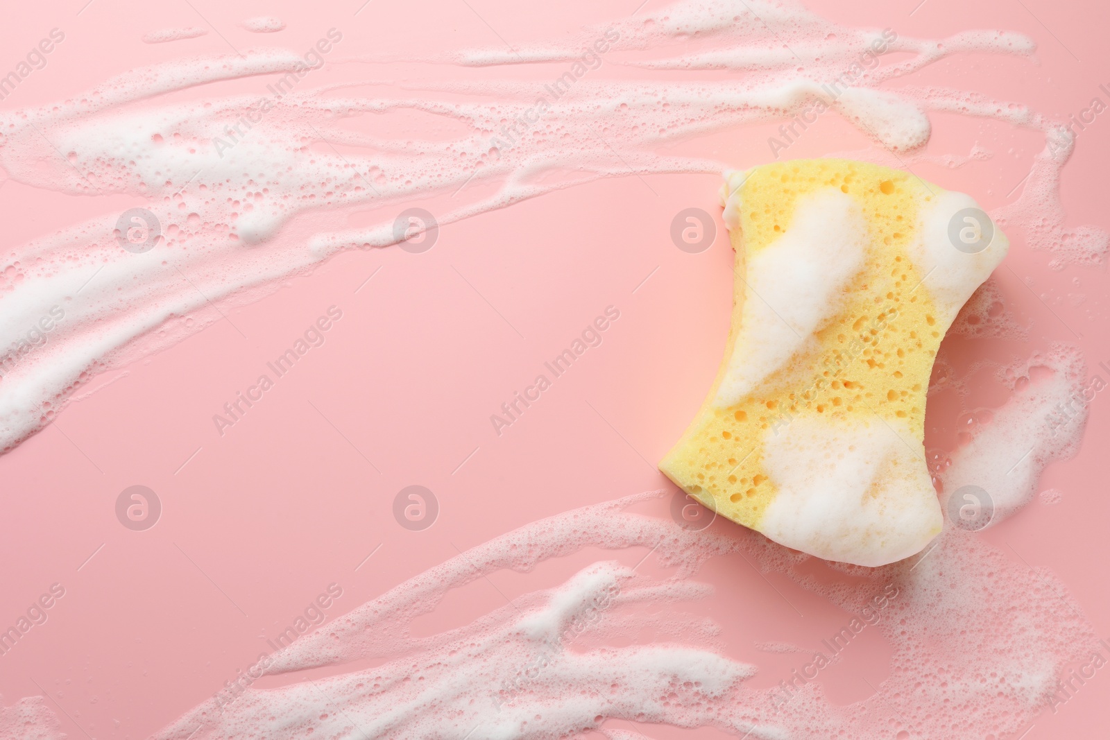 Photo of Yellow sponge with foam on pink background, top view. Space for text