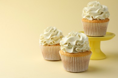 Tasty vanilla cupcakes with cream on pale yellow background, space for text