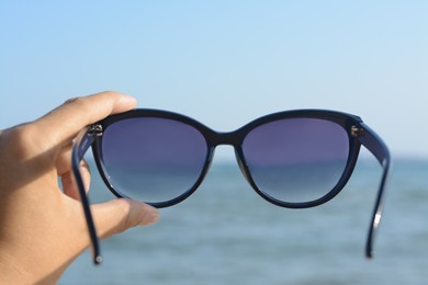 Photo of Woman holding stylish sunglasses near sea, closeup