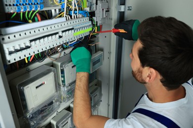 Electrician repairing fuse box with screwdriver indoors