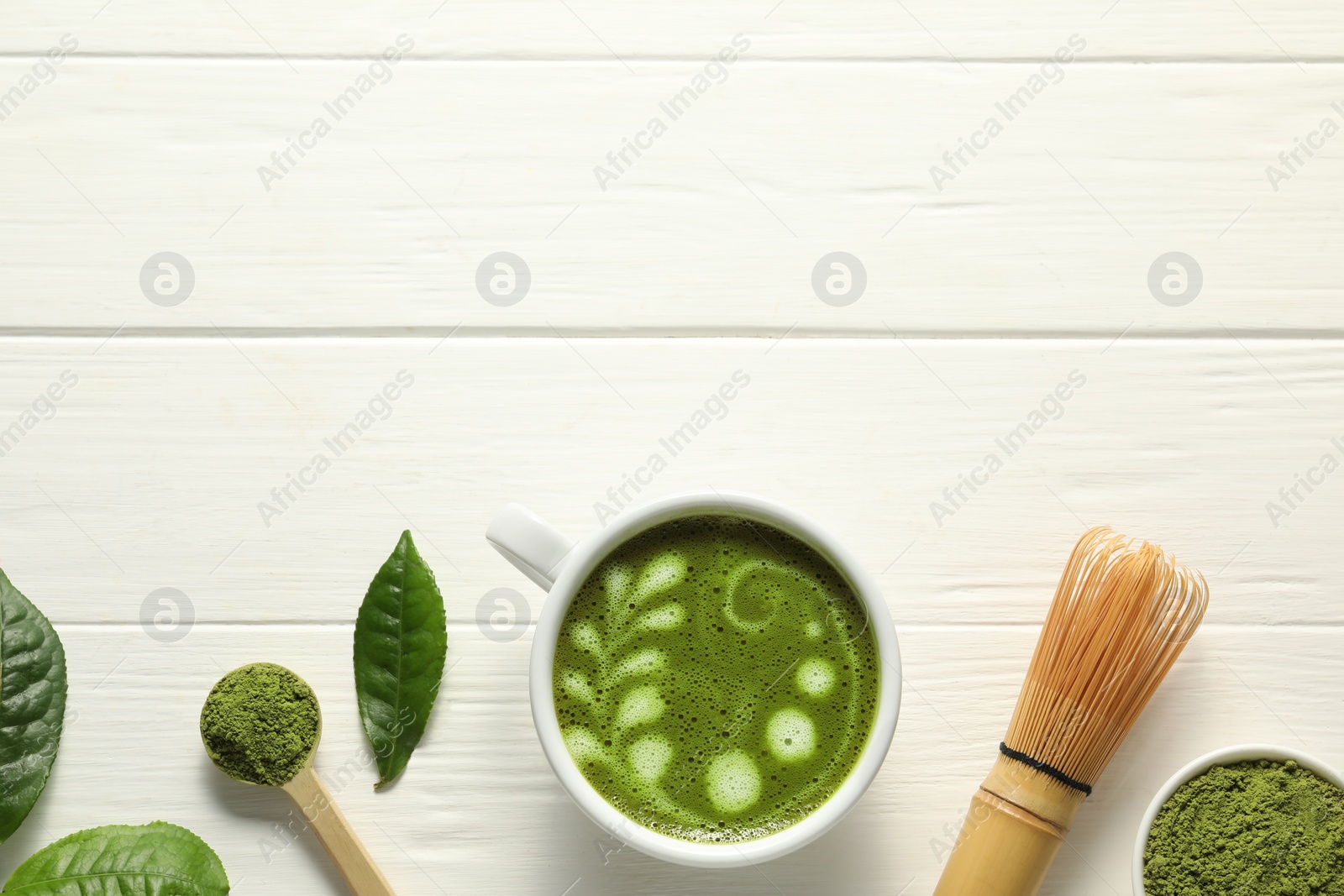 Photo of Delicious matcha latte, powder, leaves and whisk on white wooden table, flat lay. Space for text
