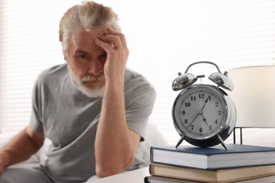 Photo of Sleepy senior man at home, focus on alarm clock