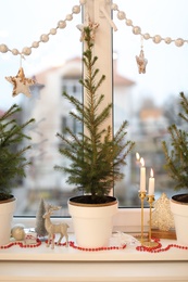 Photo of Small potted fir trees and Christmas decor on window sill indoors