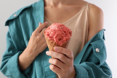 Woman holding pink ice cream in wafer cone on light grey background, closeup