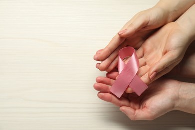 Photo of Breast cancer awareness. Women holding pink ribbon at white wooden table, top view. Space for text