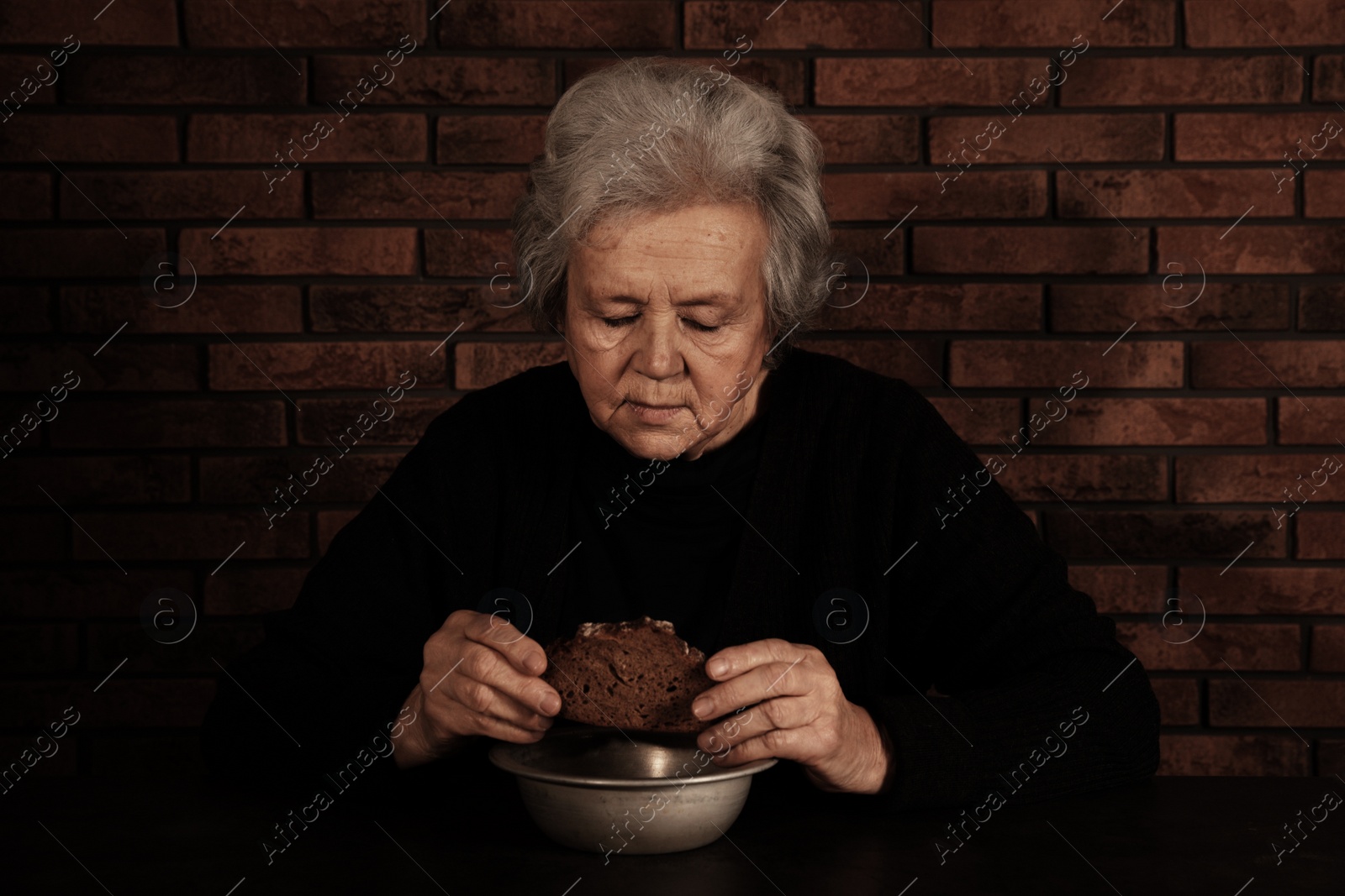 Photo of Poor mature woman with bread and bowl at table