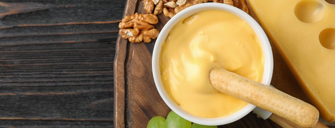 Image of Pot of tasty cheese fondue on black wooden table, top view with space for text. Banner design