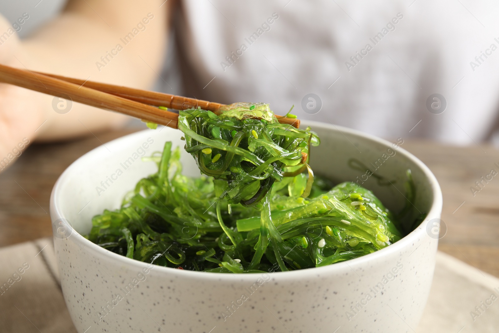 Photo of Chopsticks with Japanese seaweed salad in bowl on table, closeup