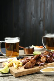 Photo of Tasty roasted chicken wings served with beer on wooden table. Space for text