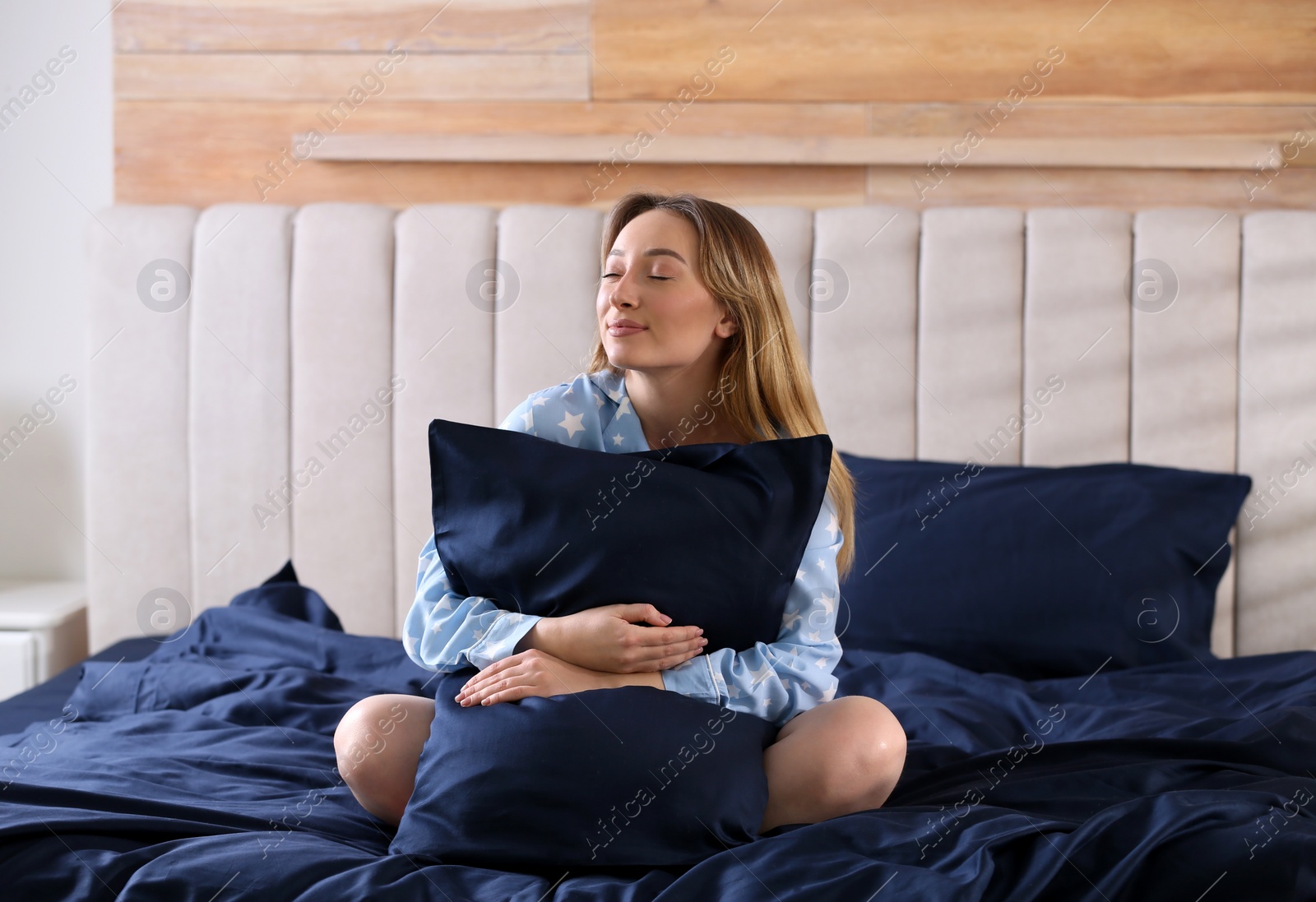 Photo of Young woman hugging pillow on comfortable bed with silky linens