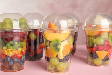 Photo of Fresh tasty fruit salad in plastic cups on pink table