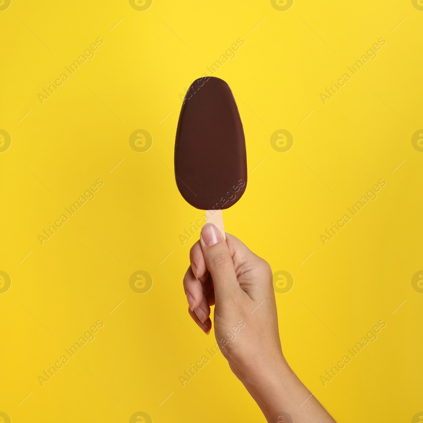 Photo of Woman holding ice cream glazed in chocolate on yellow background, closeup