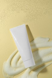 Photo of Tube of face cleanser and white foam on beige background, top view. Skin care cosmetic