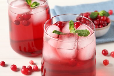 Tasty cranberry juice with ice cubes in glasses and fresh berries on white wooden table, closeup