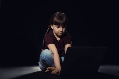 Photo of Little child using laptop on dark background. Cyber danger