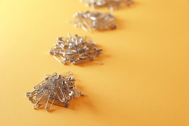 Photo of Piles of safety pins on yellow background, space for text