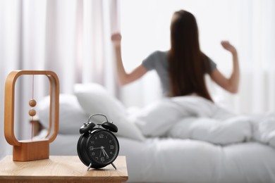 Photo of Woman stretching on bed at home in morning, focus on alarm clock. Space for text