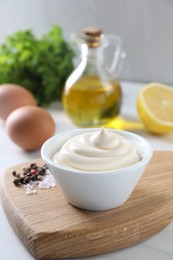 Photo of Tasty mayonnaise sauce in bowl, spices and ingredients on white table, closeup