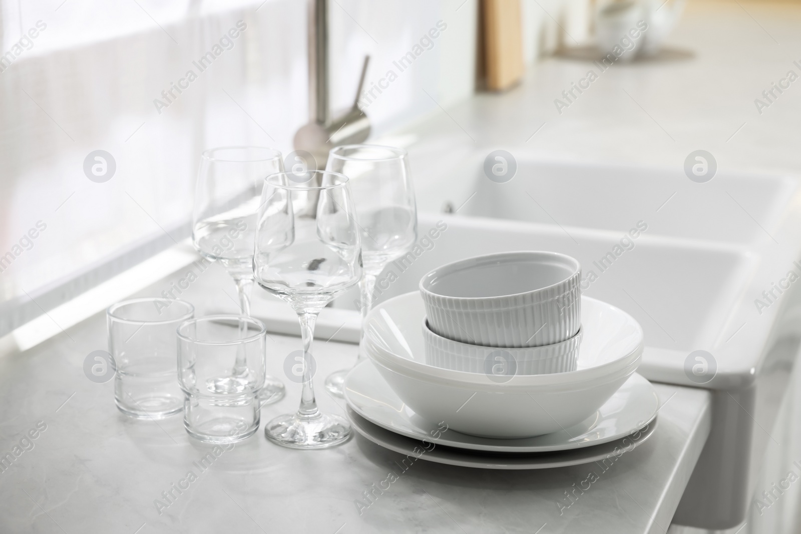Photo of Different clean dishware and glasses on countertop near sink in kitchen