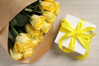 Photo of Beautiful bouquet of yellow roses and gift box on wooden table, flat lay