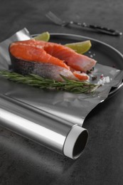 Photo of Aluminum foil with raw fish, lime, rosemary and spices on grey table, selective focus. Baking salmon