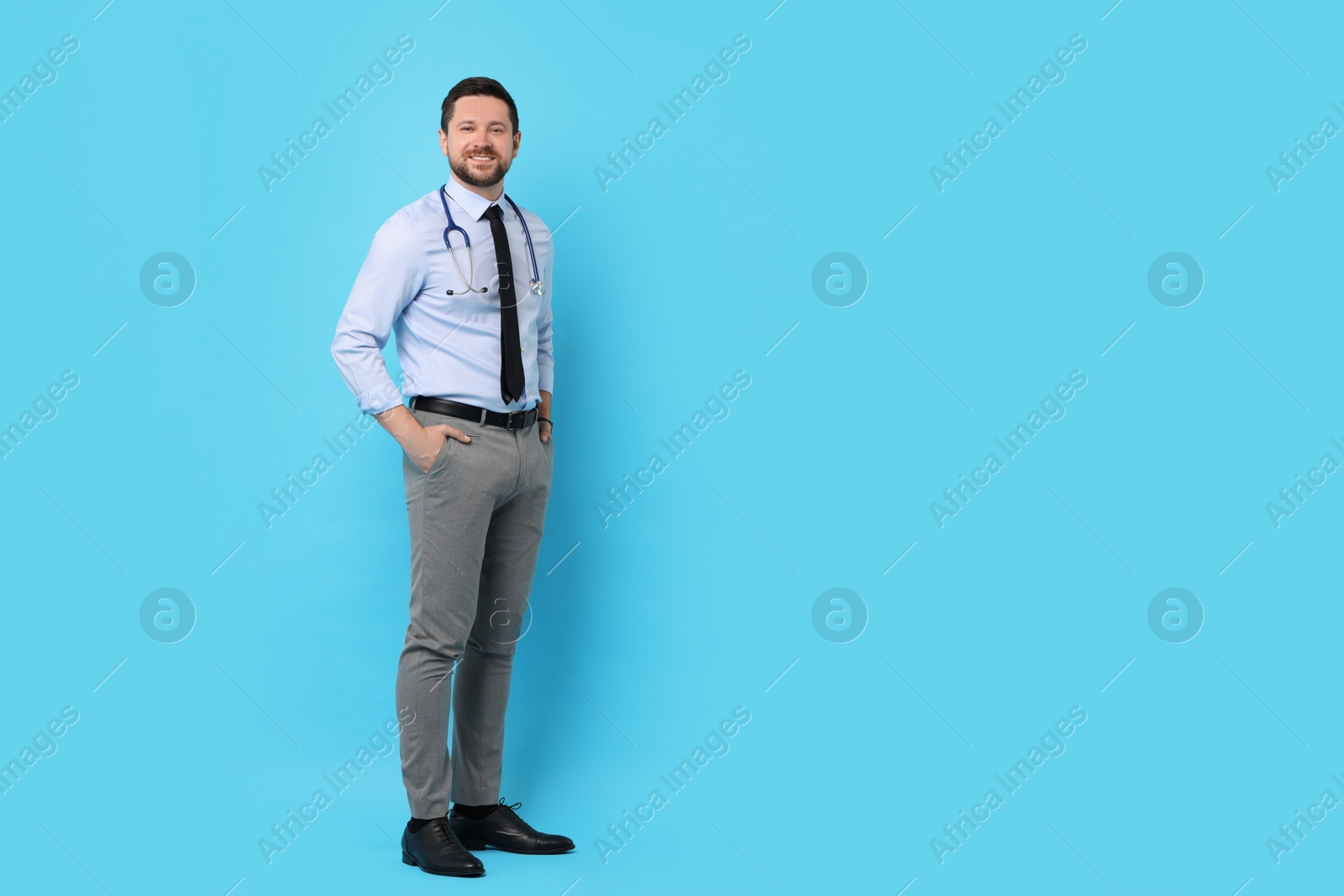 Photo of Full length portrait of smiling doctor on light blue background. Space for text