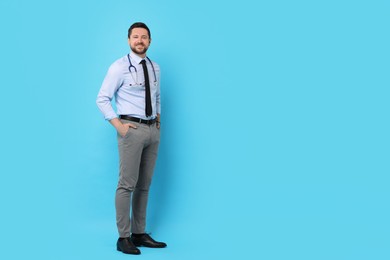 Photo of Full length portrait of smiling doctor on light blue background. Space for text