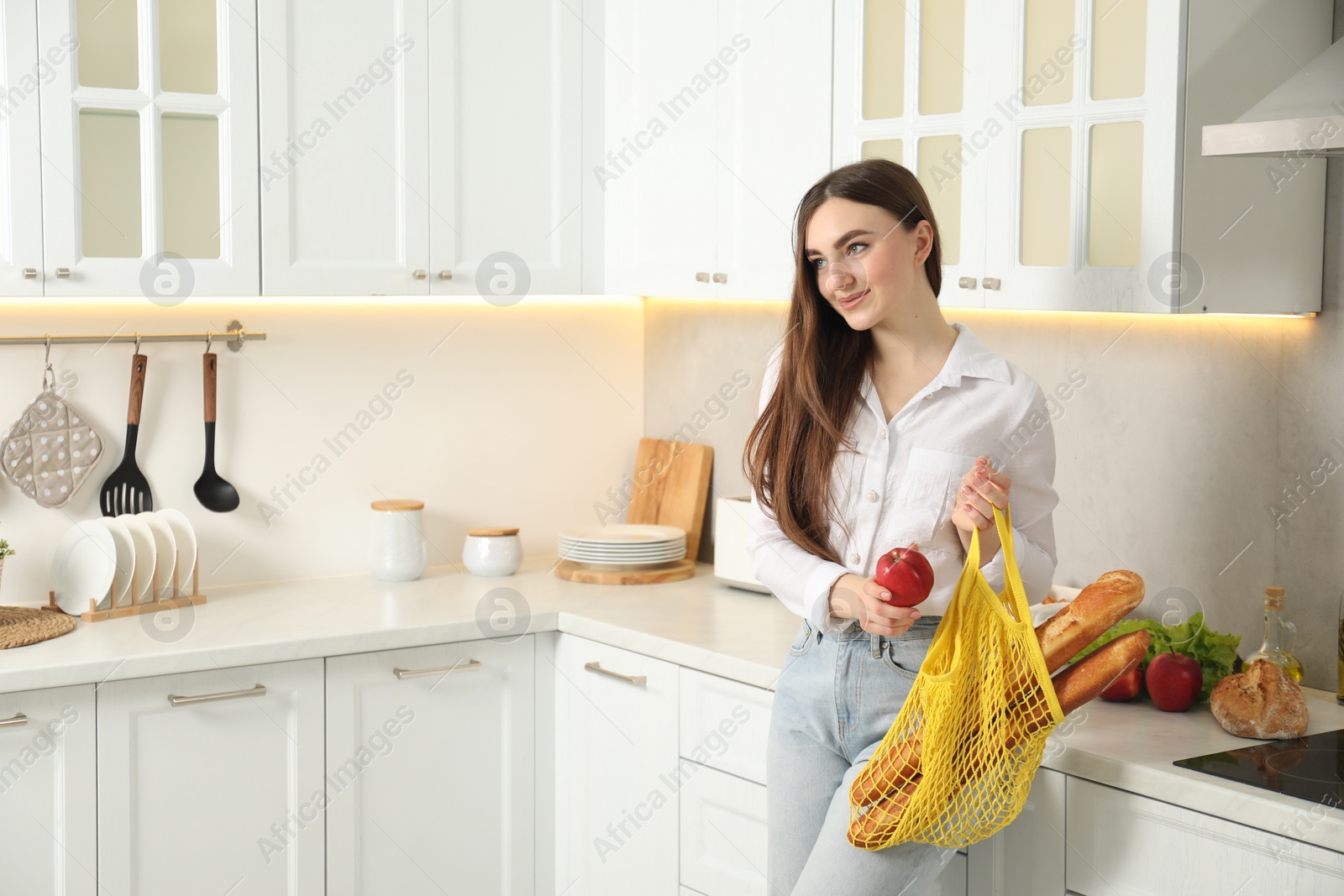 Photo of Woman with string bag of baguettes and apple in kitchen