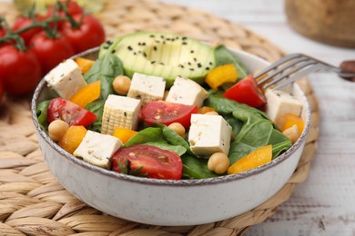 Photo of Bowl of tasty salad with tofu and vegetables on white wooden table, closeup