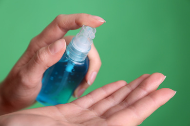 Photo of Woman applying antiseptic gel on green background, closeup