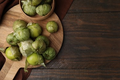 Photo of Fresh green tomatillos with husk in bowl on wooden table, top view. Space for text