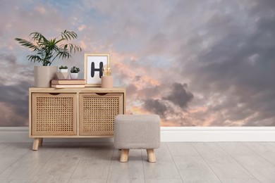 Image of Sunset sky with clouds as wallpaper pattern in room. Cabinet with decor and pouf near wall