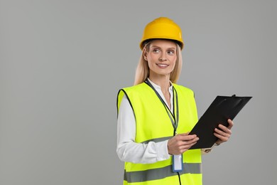 Engineer in hard hat holding clipboard on grey background, space for text