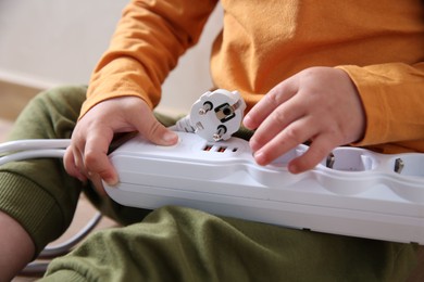 Photo of Little child playing with power strip and plug indoors, closeup