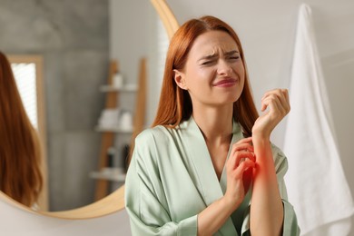 Photo of Suffering from allergy. Young woman scratching her arm in bathroom, space for text