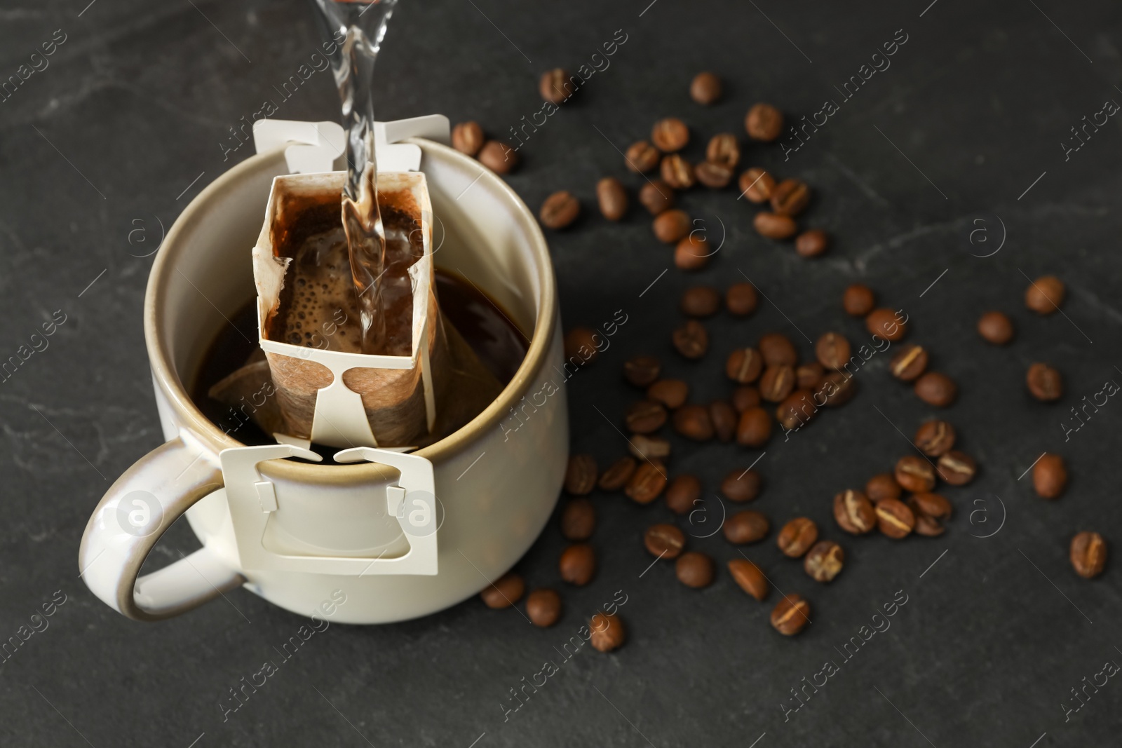 Photo of Pouring hot water into cup with drip coffee bag on black table, closeup