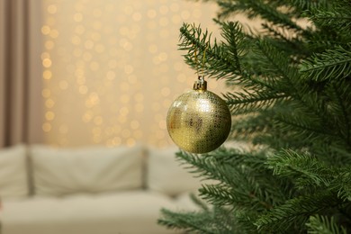 Photo of Golden bauble hanging on Christmas tree indoors. Space for text