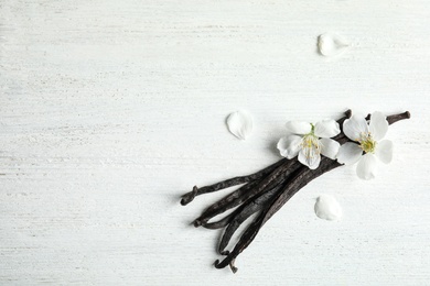 Photo of Flat lay composition with aromatic vanilla sticks and flowers on wooden background, space for text