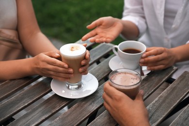 Photo of Friends drinking coffee and cocoa at wooden table in outdoor cafe, closeup