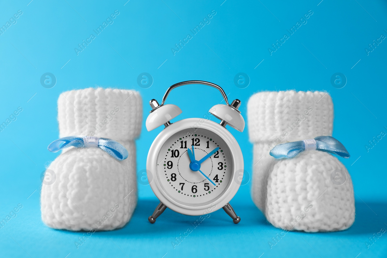 Photo of Alarm clock and baby booties on light blue background. Time to give birth