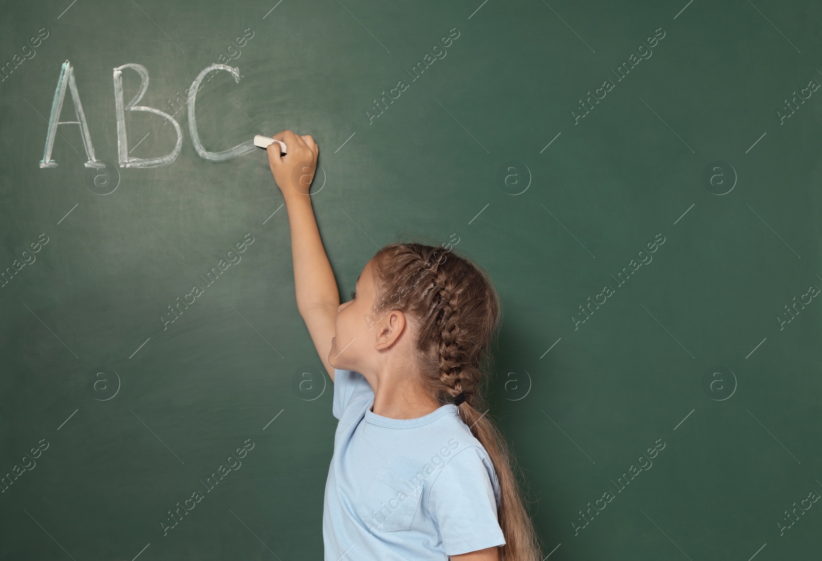 Photo of Little school child writing with chalk on blackboard