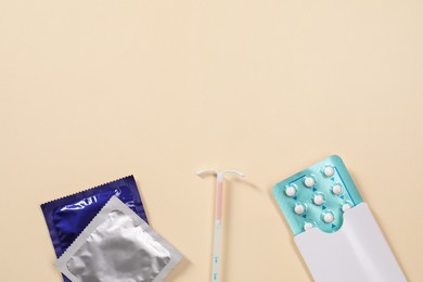 Photo of Contraception choice. Pills, condoms and intrauterine device on beige background, flat lay. Space for text