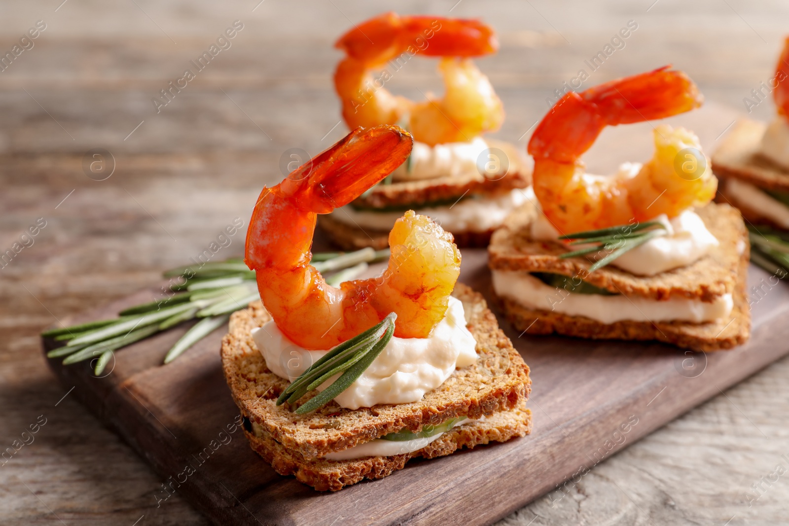 Photo of Delicious small sandwiches with shrimps on wooden board