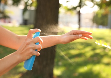 Photo of Woman applying insect repellent onto hand in park, closeup