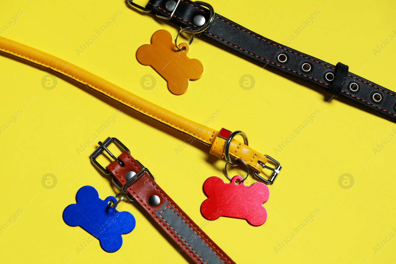 Photo of Color leather dog collars with tags in shape of bone on yellow background, flat lay