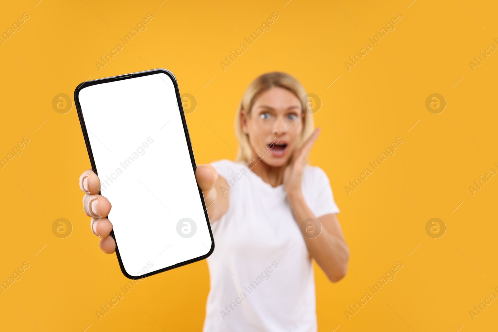 Photo of Surprised woman holding smartphone with blank screen on orange background, selective focus