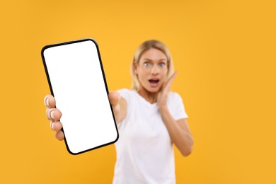 Photo of Surprised woman holding smartphone with blank screen on orange background, selective focus